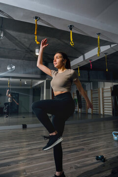 Portrait of female model performing high knee balance exercise confidently. Sporty woman improving coordination in gym, fitness training concept.