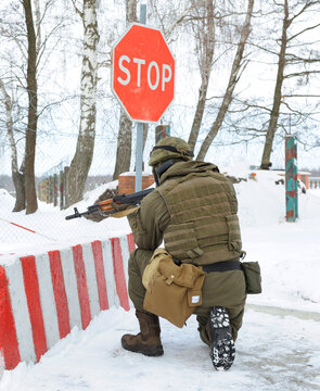 Armed Ukrainian soldier aiming Kalashnikov assault rifle near stop sign on military checkpoint