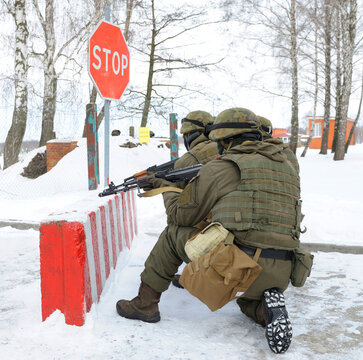 Armed Ukrainian soldiers aiming Kalashnikov assault rifle near stop sign on military checkpoint