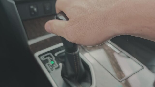 Close up of a man's hand shifting the automatic gear selector. The driver moves the lever from park to drive before starting a journey