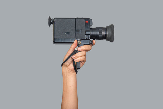 Retro video camera in hand, vintage paparazzi video recording device, isolated on gray background.