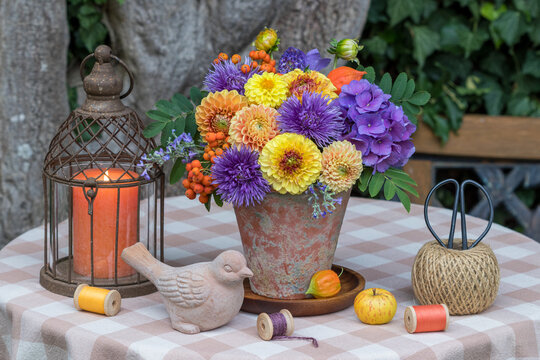 Sommer-Gartenarrangement mit Blumenstrau&szlig; mit gelben Dahlien, lila Sommerastern, Hortensienbl&uuml;ten und Ebereschenbeeren im Terracotta-Topf und vintage Laterne