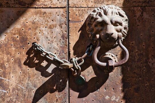 Antico battente a testa di leone con catena e lucchetto su portone di ferro arrugginito