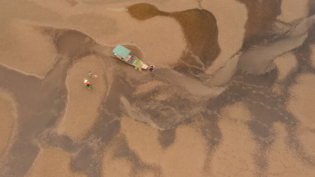  A fisherman family and their wooden boat rest on the dry riverbed during the dry season as the river runs nearly out of water. Aerial view revealing the impact of seasonal drought on traditional rive