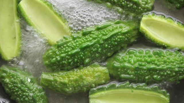 Boiling halved fresh bitter melons in bubbling water. Top view shot
