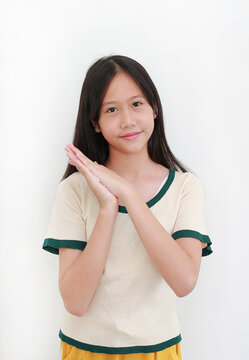 Asian girl in cream-colored t-shirt with green trim, smiling gently at the camera while holding her hands together in a polite greeting or grateful gesture against white background.