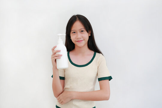 Portrait of smiling young Asian girl holding a blank white pump bottle of lotion or liquid soap, isolated on a white background.
