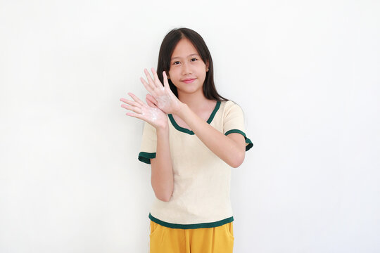 A smiling young Asian girl showing her hands covered in white soap or lotion, promoting hygiene and skincare on a white background.