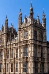 Obraz premium Detailed view of the ornate Gothic Revival architecture of the Palace of Westminster in London, England, showcasing intricate stonework, towers, and historic windows beneath a clear blue sky