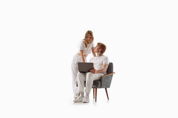 Obraz premium Young couple using laptop together while seated in armchair on white studio background. Concept of online planning, shared decisions, digital lifestyle.