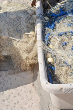 A top down shot of tangled commercial fishing nets with blue and white buoys piled inside a large plastic container on a stone dock.