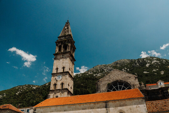 Historic bell tower of Saint Nicholas Church rising above the old town of Perast on a sunny summer day. Iconic stone architecture with mountain backdrop in Boka Bay.
