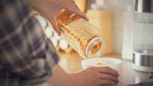 In bright morning kitchen, woman's hands scoop measured corn flakes into bowl, sunlight streams through window, embodying home cooking routines that promote balanced nutrition and healthy lifestyle