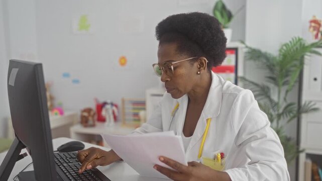 Woman in lab coat types on keyboard and holds medical papers with hands while checking notes at desk in building; concentration medical care.