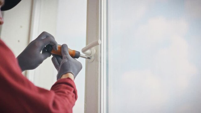 A close-up of a screwdriver in a technician's gloved hands adjusting plastic window hardware in a home environment. Concept of DIY repair and independent adjustment of plastic windows