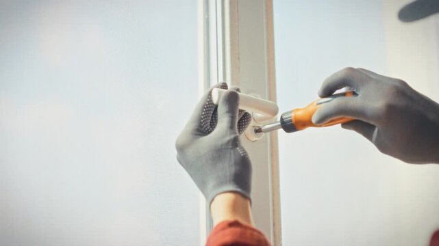 A close-up of a technician's gloved hands unscrewing plastic window fasteners with an orange screwdriver. Concept of technical maintenance and replacement of worn window hardware elements