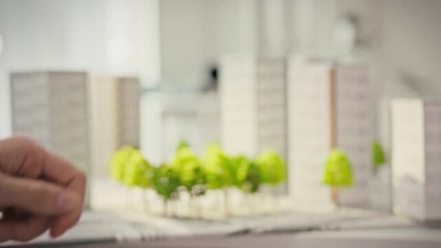 A close-up of female hands passing keys to a male client in a modern real estate office surrounded by miniature models of residential complexes. Concept of handing over a new home