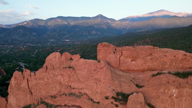 Aerial view flying parallel with large orange rock cliff with mountains in the background