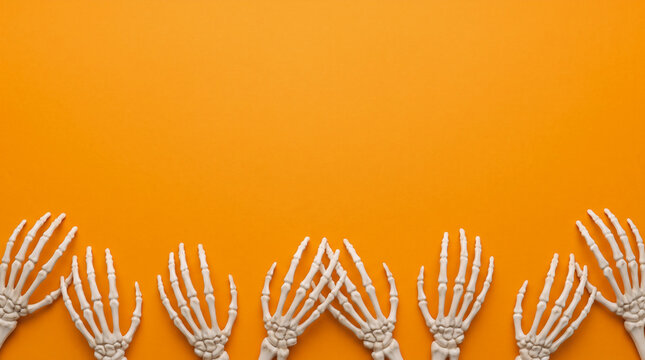 Halloween orange background with creepy skeleton hands rising along the bottom border, large copy space for scary Halloween party decoration, horror backdrop and eerie gothic design