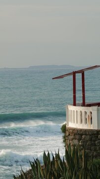Vertical 4K 50fps real-time footage of a coastal viewpoint overlooking Atlantic waves with the distant Berlengas Islands on the horizon in Santa Cruz, Portugal