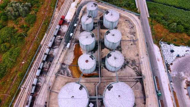 Top view of circular storage tanks and railway track. Overhead shot reveals round industrial containers positioned along train tracks with cargo cars.
