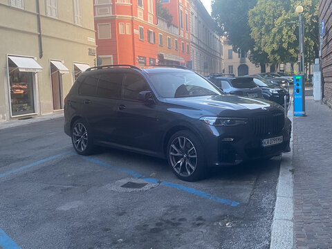 Dark BMW X7 SUV parked on Piazza Guglielmo Marconi in Cremona, Italy, near electric charging station