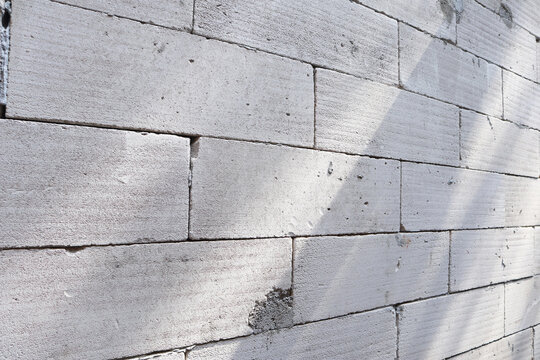 Light gray lightweight concrete block wall texture with diagonal shadows and sunlight. AAC brick wall