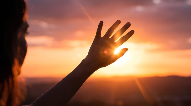 Hand silhouette reaching toward golden sunset sky.