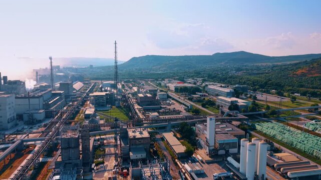 Industrial plant with gas storage cylinders and pipelines. White vertical tanks sit beside factory buildings under bright sunlight.
