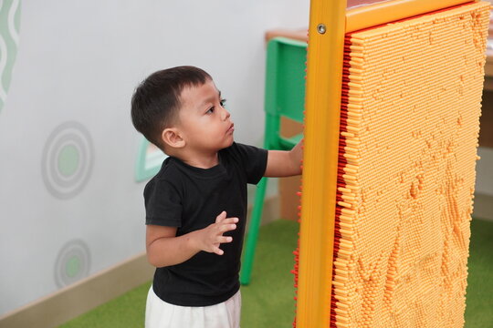 Asian toddler boy touching pin screen board sensory interactive toy inside indoor playground