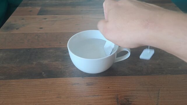 Placing a tea bag into a white mug.