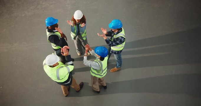 Top view, construction and team huddle with hands together for support, success or solidarity at job site. People, architect stack and excited renovation with applause, high five and unity with space