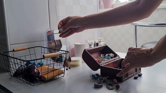 Hands organize jewelry in a small wooden box in a bright room during the day