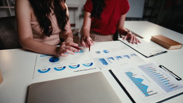Two female colleagues analyzing financial charts and statistics together. They are planning a business strategy and discussing the market report