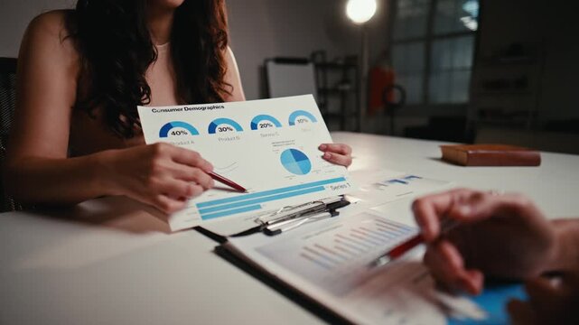 Two business professionals discussing financial data and consumer demographics in an office meeting, pointing at charts and graphs