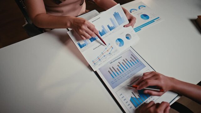High-angle view of two businesswomen analyzing financial charts and graphs during a meeting, discussing sales performance and growth