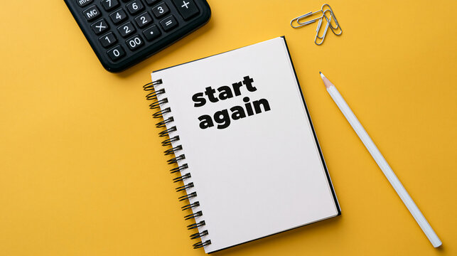 A spiral notebook with text start again sits on yellow surface with calculator. Conceptual image for life changes and.