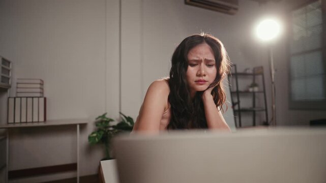 Emotional young woman feeling sad and crying while watching a drama or tragic movie on her laptop computer alone at home late at night