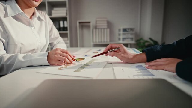 Two business professionals analyzing statistical data and financial graphs on documents. Colleagues collaborating on a marketing project in the office