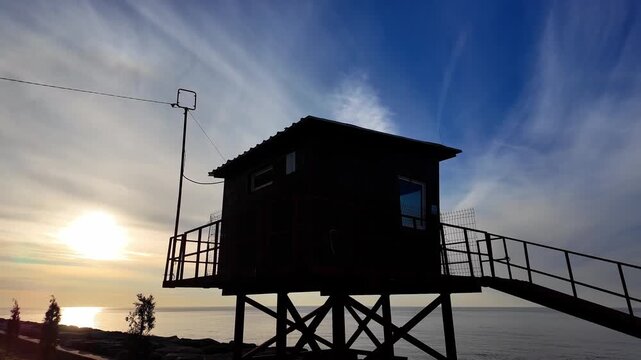 Wooden observation deck on stilts silhouetted against golden sunset sky over batumi coastline.