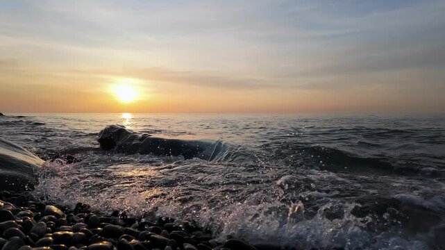 Gentle waves wash over pebble beach rocks as sun sets on batumi coast horizon.