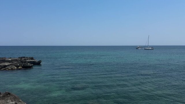 People enjoy swimming and paddleboarding in clear turquoise waters while yachts and motorboats anchor offshore near Monopoli. Summer vacation, coastal tourism, seaside recreation, Mediterranean travel