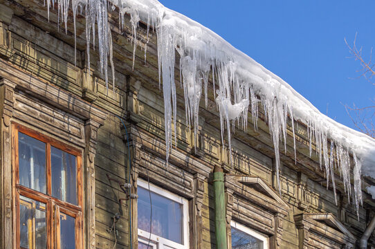 Large icicles of ice on the roof of an old wooden house. An old wooden barracks. Moldy wooden planks of the walls of an old house.