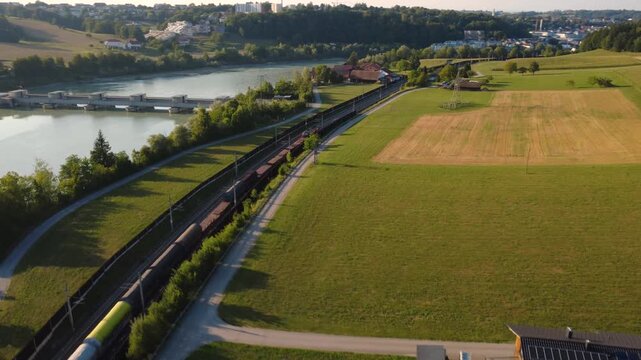 Aerial view of a freight train travelling along the river Inn past a hydropower plant