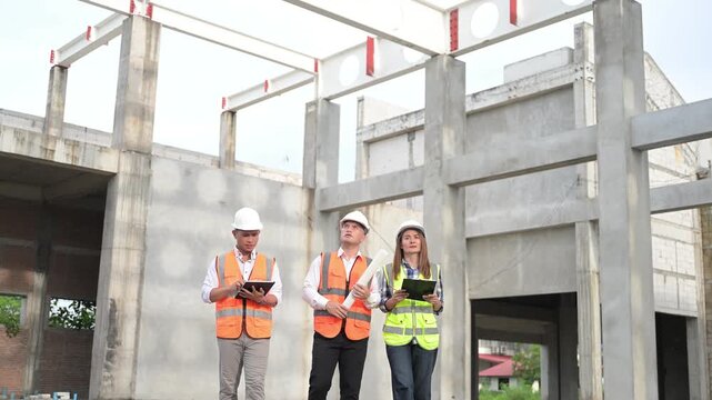 Construction engineers review a blueprint and discuss project plans at a building site. Concept of civil engineering, teamwork, architecture, construction management, and development.