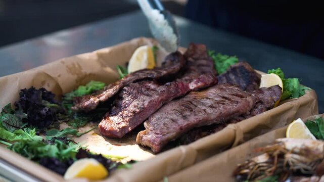 Grilling meat. Grilling meat outdoors with fresh herbs and lemon at a barbecue gathering. People are grilling meat outdoors during a barbecue gathering. Fresh herbs and lemon slices are placed on a tr