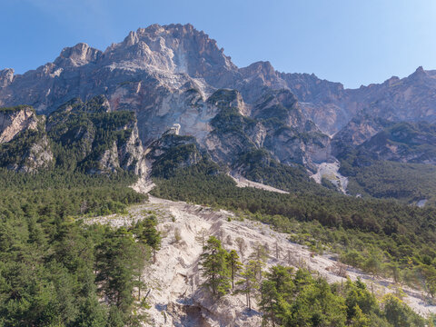 Aerial view of a mountain landslide and debris flow on the slopes of the Dolomites, showing exposed rock, eroded soil, and surrounding pine forests in Cortina d'Ampezzo, Veneto, Italy.