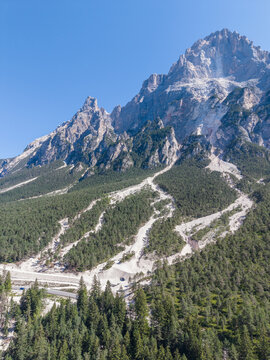 Aerial view of a mountain slope in the Dolomites showing visible debris flow channels and rockfall paths cutting through the dense pine forest near Cortina d'Ampezzo, Veneto, Italy.