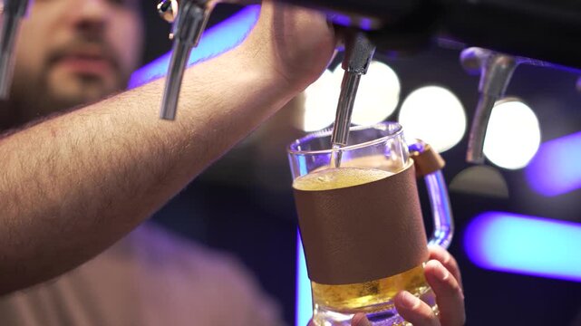 Bartender pours drink in a busy bar during the evening hours. A bartender serves a beer from the tap at a bar. The setting is lively with customers enjoying their time. The action happens at night wit