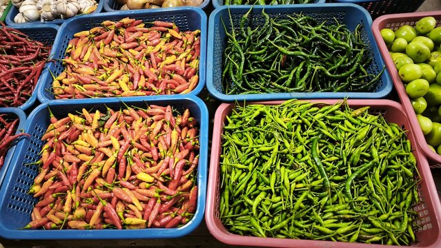 View of a vibrant market stall displaying baskets of fresh ginger, red chilies, garlic, limes, and onions